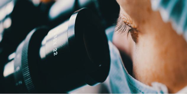 An image of a woman wearing a mask, looking through a microscope