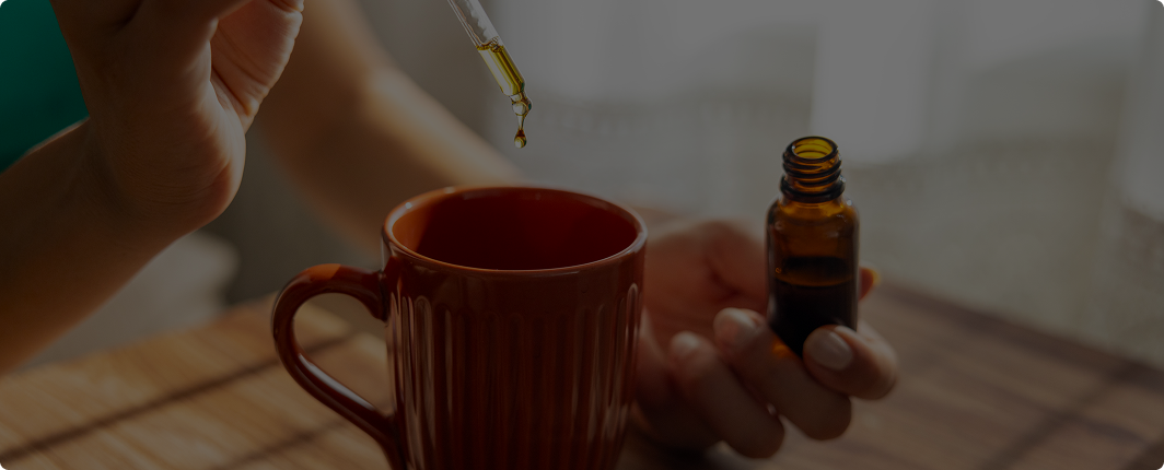 Person holding an amber CBD oil dropper bottle over a mug